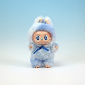 A 3D render of a cute, standing, collectible character wearing a light blue and white two-tone fluffy costume with bunny ears and a dark blue bow tied at the neck. The character has large, round blue eyes and a mischievous smile showing tiny teeth. It is set against a soft white and light blue gradient background.
