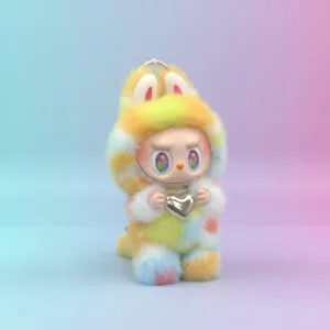 A digital illustration of a small, stylized character wearing a fluffy, rainbow-colored bunny suit. The suit features shades of yellow, orange, blue, and pink. The character has large, expressive eyes with colorful irises and is holding a shiny, silver heart-shaped pendant on a chain. The background is a smooth, gradient blend of soft blue and pink.