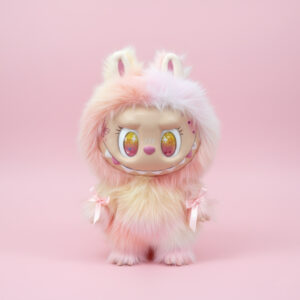 A 3D render of a cute, furry character in a pastel pink and yellow ombré fluffy costume with bunny ears and small pink bows on its wrists. The character has large, expressive, golden-yellow eyes with star reflections and a wide, mischievous smile with visible teeth. It is set against a solid light pink background.